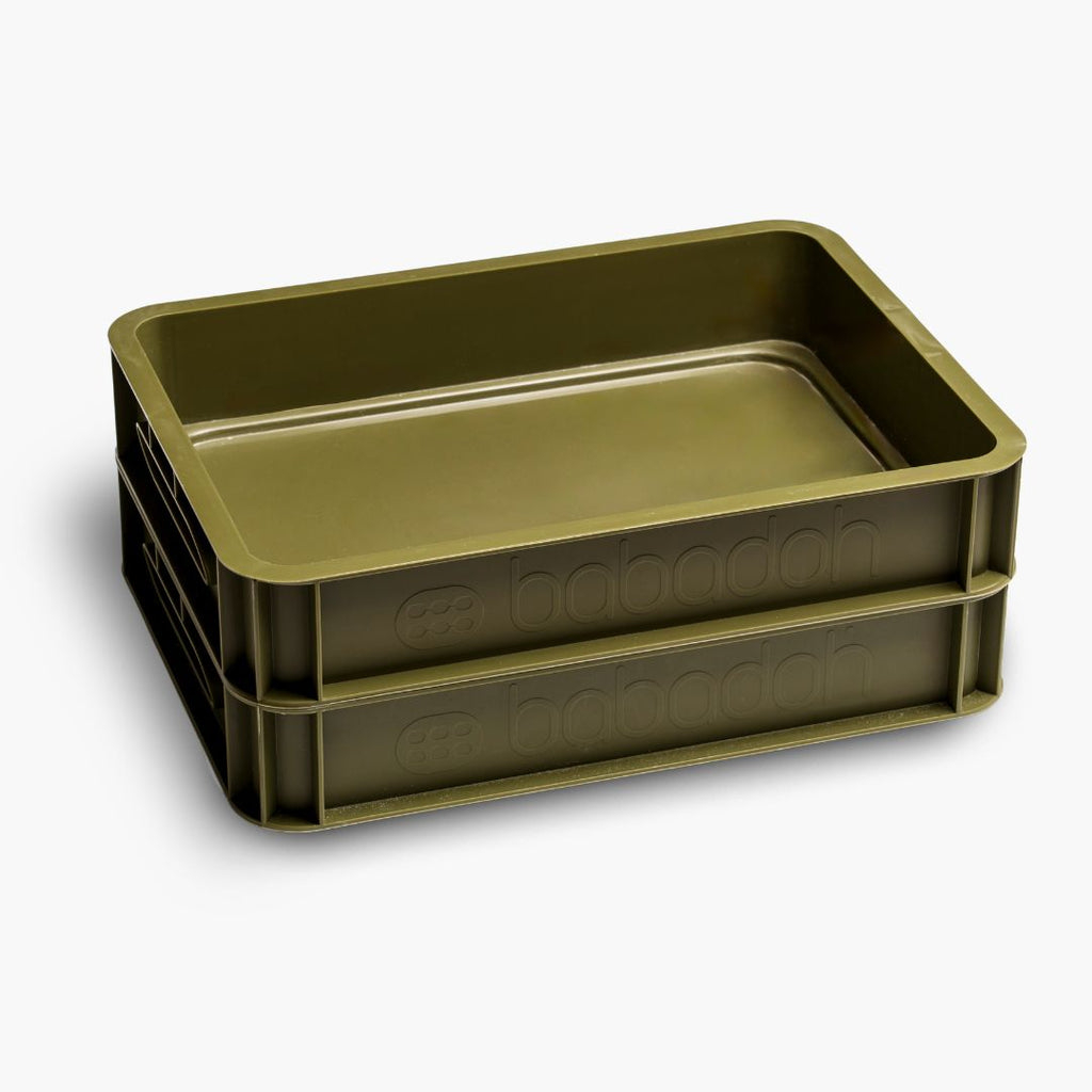 A side-on view of two empty olive-green dough trays with a smooth, glossy surface, slightly raised edges and the words 'Babadoh' along the side.
