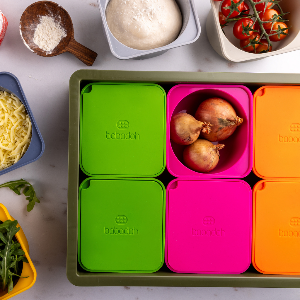 A top down view of brightly coloured containers with the brand name 'Babadoh'. One container is holding some onions.