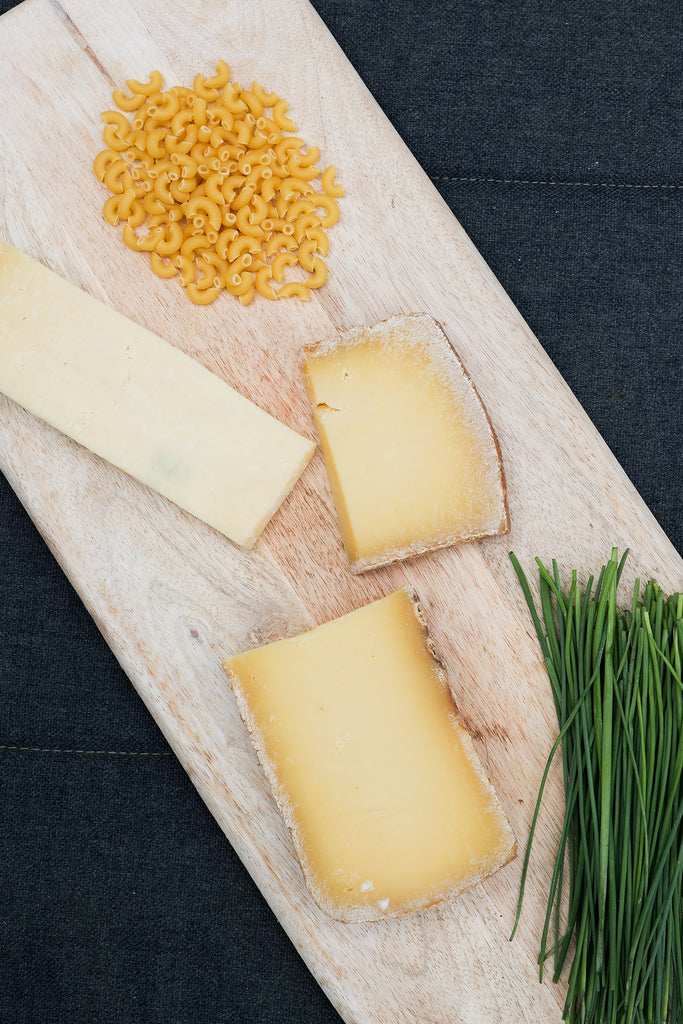 Wooden board with a selection of cheese and pasta to make macaroni cheese