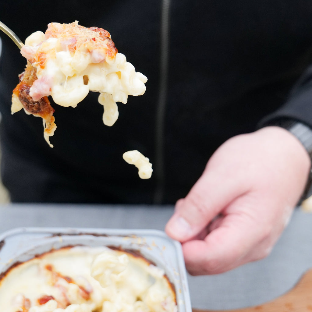 Hands serving up a spoon full of macaroni cheese