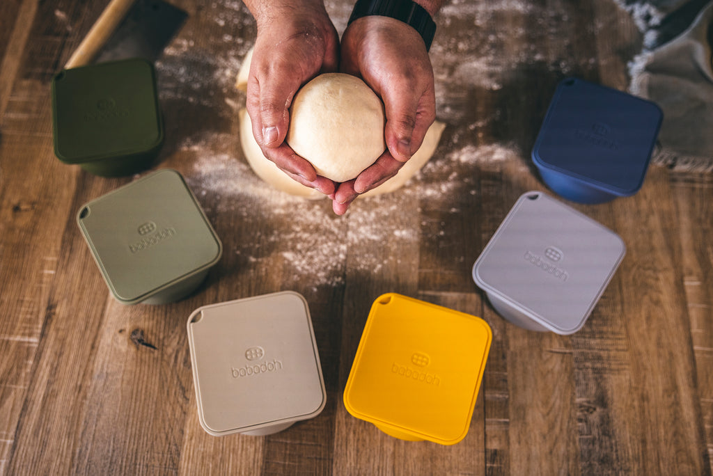 hands holding pizza dough ball with babadoh proving containers